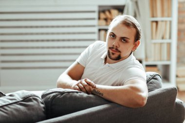Yakışıklı adam evdeki kanepede oturuyor.