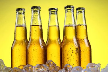 Sarı arka planda köpüklü bira şişeleri.