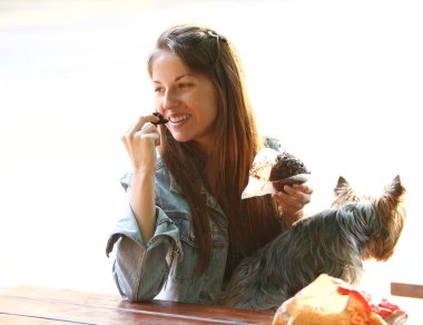 Güzel bir kadın köpeğiyle parkta dolaşırken yemek yer.