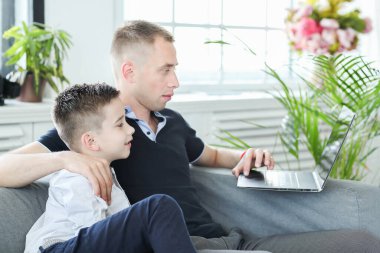 Baba ve oğul evde dizüstü bilgisayardan film izliyorlar.