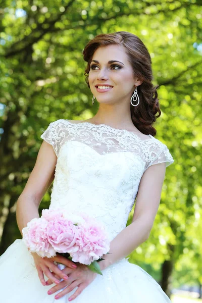 年轻美丽的新娘拿着一束鲜花在公园里摆姿势 — 图库照片