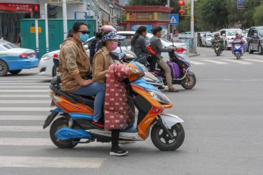 İki Tibetli kadın yüz maskesi ve gözlük takıyor Lhasa 'da motosiklet sürüyorlar yaya geçidinde duruyorlar ve ellerinde ulusal giysiler var.