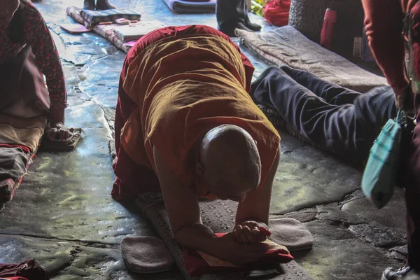 Geleneksel kırmızı ve sarı giysiler içinde yaşlı bir keşiş Barkhor Meydanı, Tibet 'teki Jokhang Tapınağı önünde secde ederek dua ediyor.