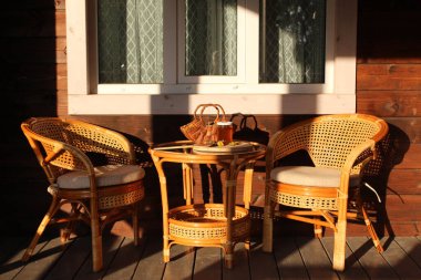 İki sandalye ve veranda seti. Kavanozda karahindiba reçeli ve masada ahşap karahindiba sepetinden çiçekler..