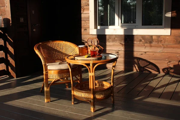 Krzesło i stół patio w promieniach wieczornego słońca. Słoik dżemu, filiżanka herbaty i kosz kwiatów mniszka lekarskiego — Zdjęcie stockowe