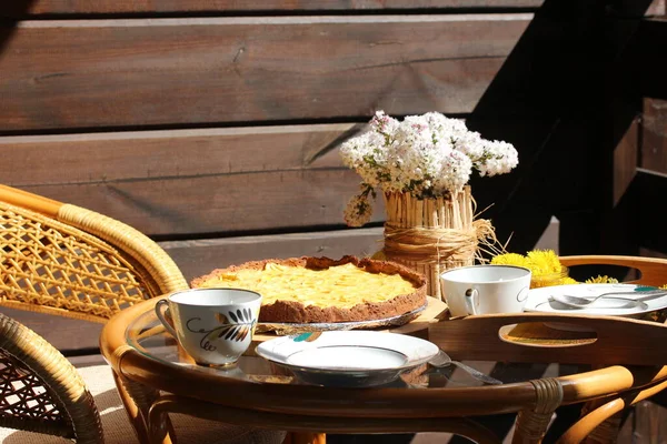 Herbaciana impreza na słonecznym patio. Tarta jabłkowa i wazon z kwiatami na stole. — Zdjęcie stockowe