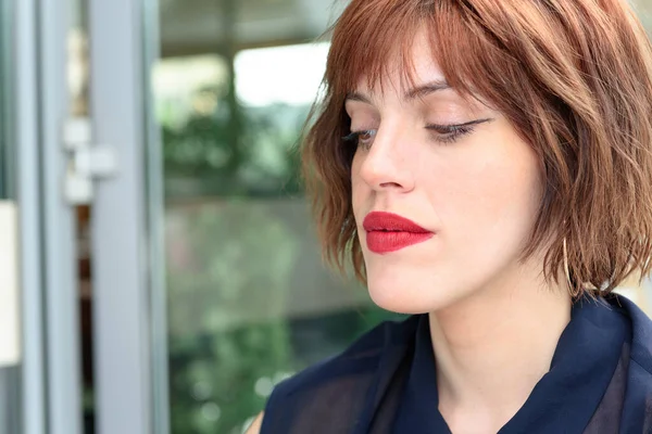 Kızıl Saçlı Kız Portresi. Dudaklarında kırmızı ruj var. Şehir arkaplanı.