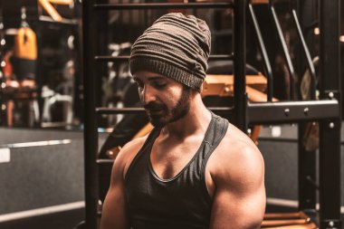 Kaslı, yorgun vücut geliştiren adam spor salonunda otururken ya koşuya ya da egzersize ara verdiğini gösteriyor. Fitness genç sporcusu antrenmanda dinleniyor. Sağlıklı bir şekilde çalış..