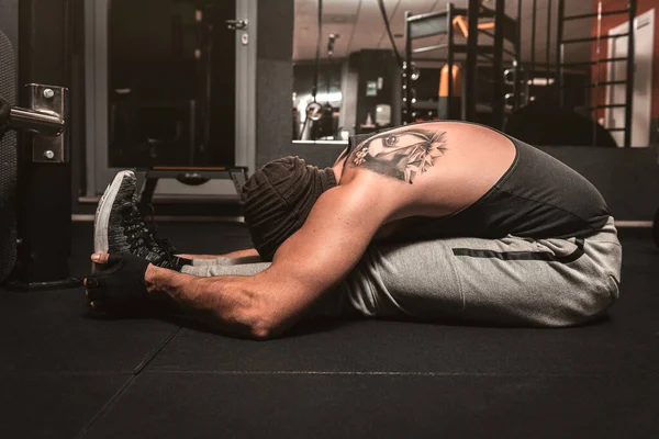 A sporty man in the gym is doing Yoga exercises. Paschimottanasana position: forward bending when seated. Yoga mental benefits.