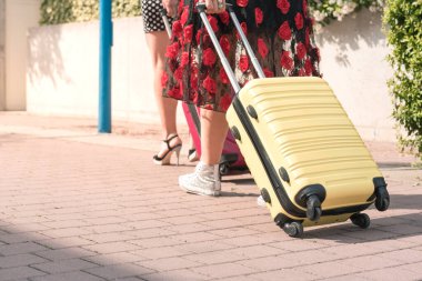 Şehrin çiçekli caddesinde bavullarıyla yürüyen iki zarif turist kadının kesilmiş fotoğrafı..