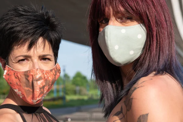 Two women with colorful masks in the summer city look directly into the camera.