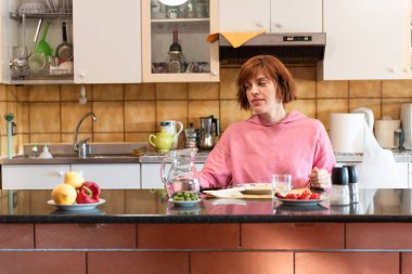 Genç ve güzel bir kadın mutfağında tek başına yemek yiyor..