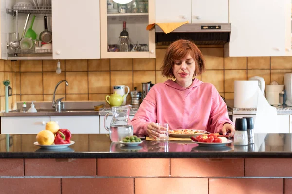 Genç ve güzel bir kadın mutfağında yemek yer ve bardaktan su içer..