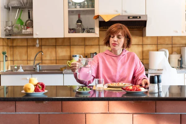 Genç ve güzel bir kadın mutfağında yemek yer ve bardağa su döker..