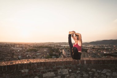 Kadın gün batımında yoga ya da pilates yapıyor ya da güzel bir şehirde gün doğumunda..