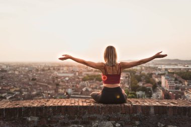 Kadın gün batımında yoga ya da pilates yapıyor ya da güzel bir şehirde gün doğumunda..