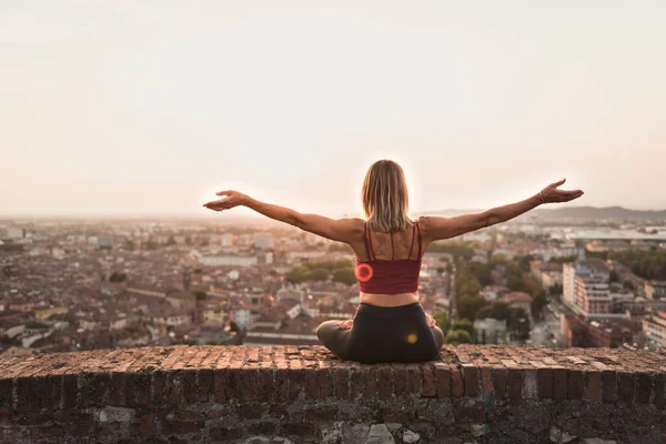 Kadın gün batımında yoga ya da pilates yapıyor ya da güzel bir şehirde gün doğumunda..