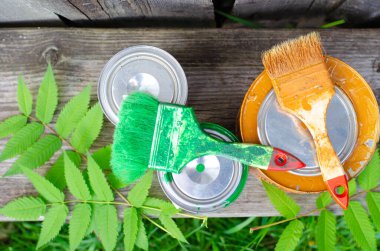 Boya fırçaları ve ahşap bir bankta üzerinde mavi ve kahverengi boya bulunan teneke kutular fotokopi alanı olan düz bir zemin üzerinde yatıyordu. ÇEVİR