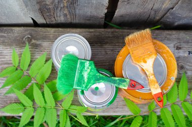 Boya fırçaları ve ahşap bir bankta üzerinde mavi ve kahverengi boya bulunan teneke kutular fotokopi alanı olan düz bir zemin üzerinde yatıyordu. ÇEVİR