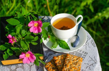 Bir fincan yeşil çay, bir nane yaprağı, çiçekler ve bahçede bir masanın üzerinde bir kitap. Yaz köyü konsepti. Pankart.