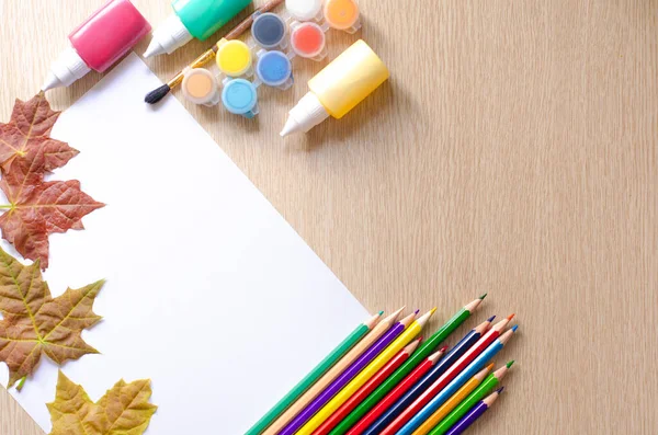 Kleurpotloden, verftubes, schilderdoek en herfstbladeren op houten bureau. Terug naar school en kunstconcept. — Stockfoto