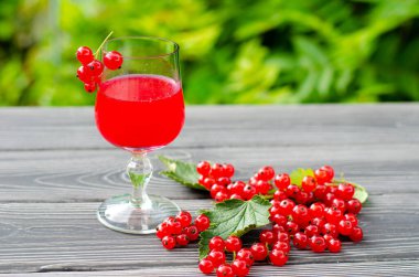 Taze kırmızı üzümlü içecek ve yeşil bahçedeki ahşap masada sulu böğürtlen..