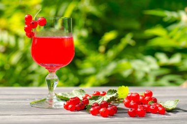 Taze kırmızı üzümlü içecek ve yeşil bahçedeki ahşap masada sulu böğürtlen..