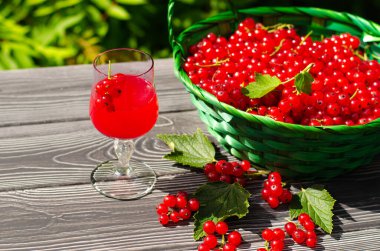 Taze kırmızı üzümlü içecek ve yeşil bahçedeki ahşap masada sulu bir sepet çilek..