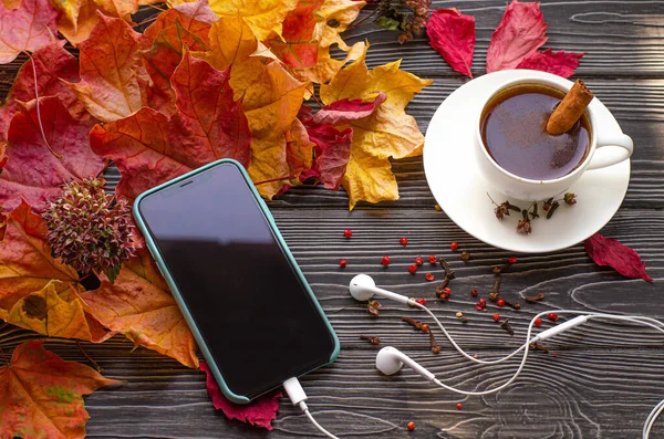 Kopp kaffe med kryddor - kanel, kryddnejlika och peppar. Hösten fallit lönn blad och telefon på en trä bakgrund. Stockbild