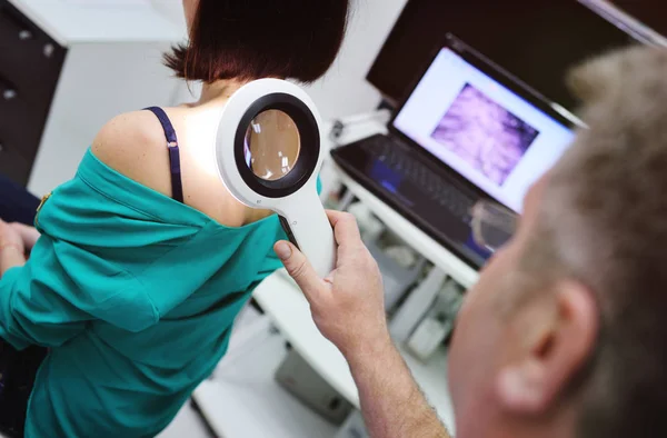 De dermatoloog onderzoekt de mollen patiënten met behulp van een speciale electorale Vergrootglas. — Stockfoto