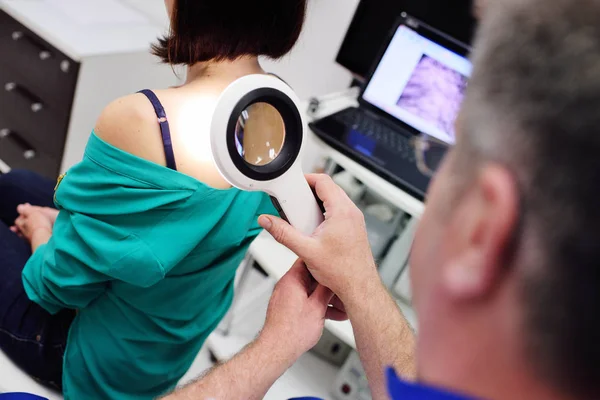 O médico examina as marcas de nascença do paciente através de uma lupa — Fotografia de Stock