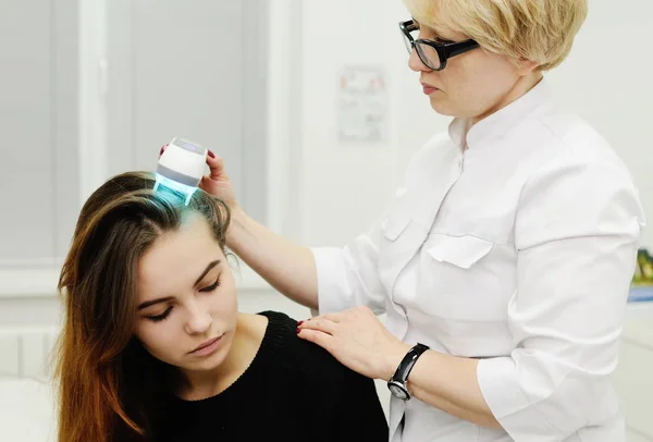 El médico examina el cuero cabelludo de un dispositivo especial con una lámpara UV — Foto de Stock