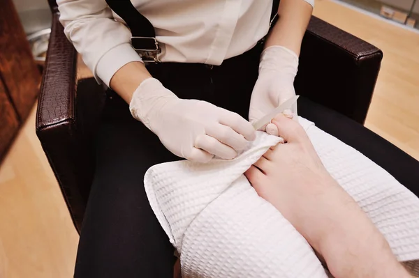 Una chica joven hace una pedicura hombre en el fondo de un salón de belleza . — Foto de Stock