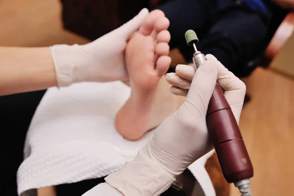 Uma jovem faz um homem pedicure no fundo de um salão de beleza . — Fotografia de Stock