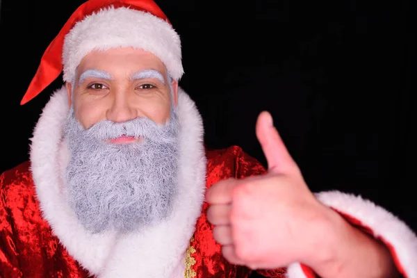 Papai Noel em um fundo escuro sorri para a câmera e mostra o polegar da mão — Fotografia de Stock