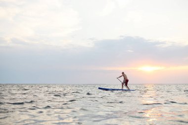 Bir adam bir Sup tahta deniz arka planı üzerinde duruyor