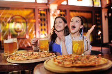 Genç güzel kızları pizza yemek, bira ya da bir bira kokteyl içme ve futbol izliyor
