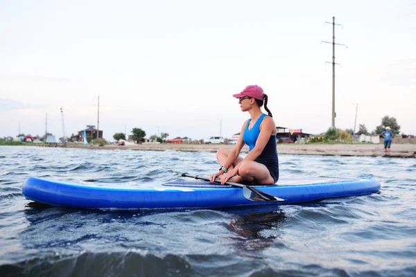 Giovane ragazza in abbigliamento sportivo seduta su un tabellone SUP — Foto Stock