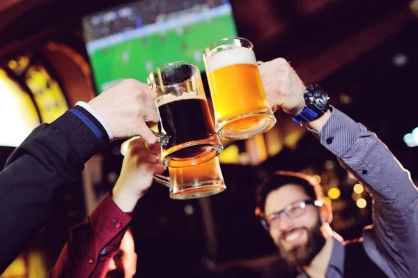 a group of young mens friends in a bar or pub drinking beer with glasses and watching football