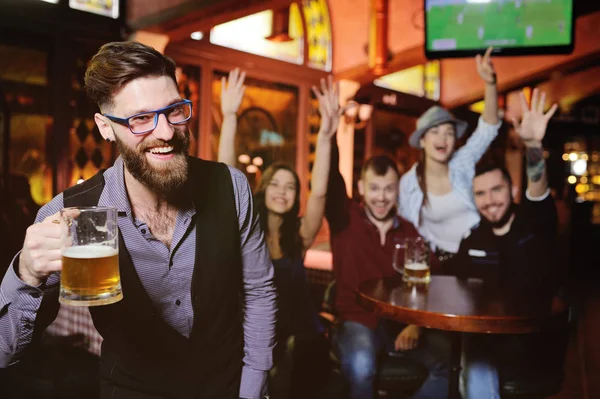 group or company of friends - young guys and girls holding glasses of beer, watching football, laughing and smiling