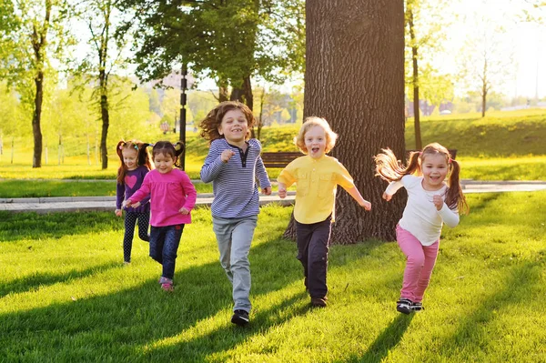 Група маленьких щасливих дітей проходить через парк на фоні трави і дерев . — стокове фото
