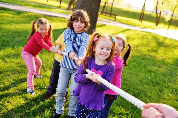 Un grupo de niños preescolares pequeños juegan un tirón de la guerra en el parque . — Foto de Stock