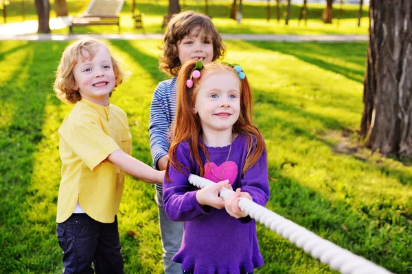 En grupp av små förskolebarn spela en dragkamp i parken. — Stockfoto