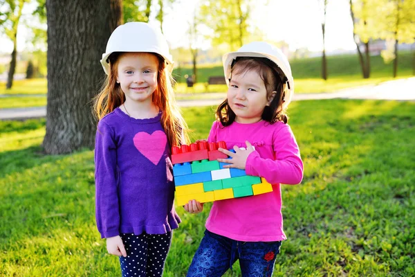Niñas lindas en cascos de construcción blancos jugando en los niños diseñador en el parque — Foto de Stock