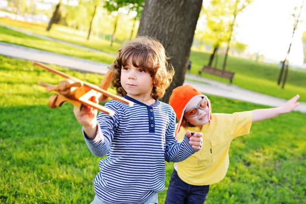 Jongens met krullend haar spelen een houten speelgoed vliegtuig in het park. — Stockfoto