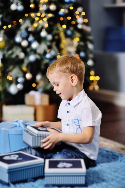Мальчик открывает коробки с подарками под елкой — стоковое фото