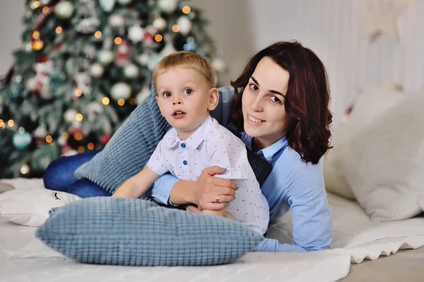 Madre con su pequeño hijo acostado en la cama sobre el fondo de un árbol de Navidad — Foto de Stock