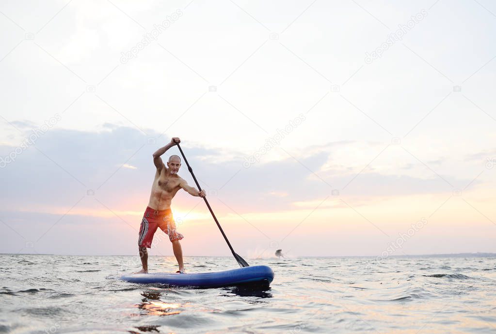 A man stands on a SUP board against the background of the sea