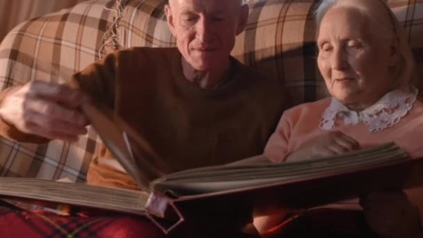 An elderly couple is considering a family photo album wrapped up in a plaid — Stock Video