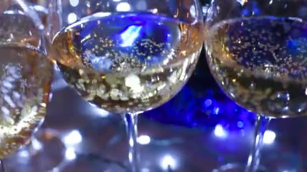 Schöne Gläser mit Champagner oder Wein auf einem Tisch vor dem Hintergrund der Weihnachtsbeleuchtung. — Stockvideo
